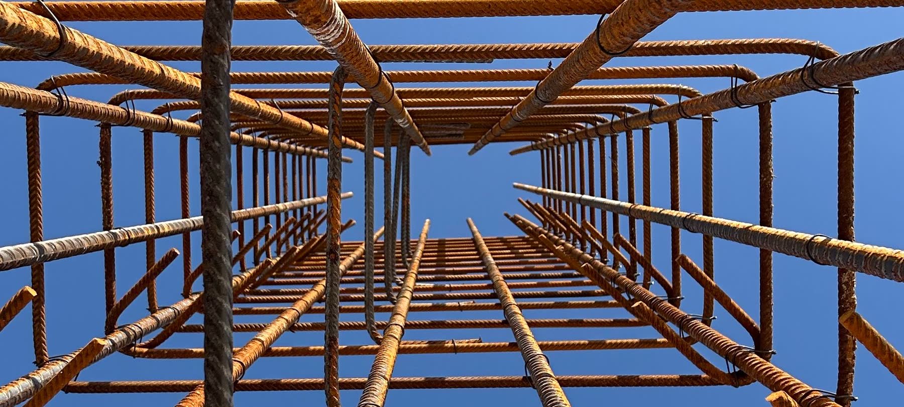 A steel reinforcing cage seen from below against the sky